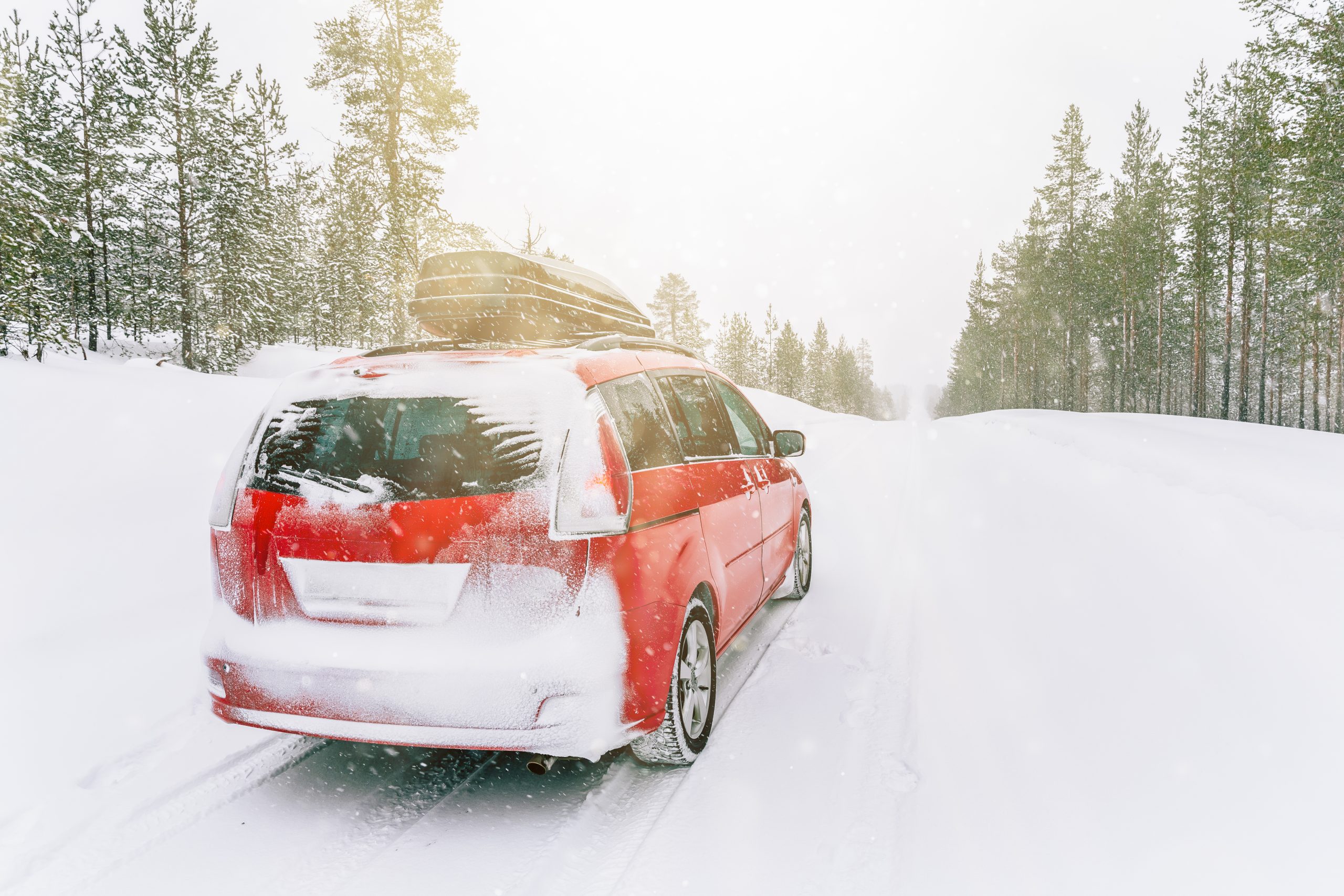 Red car with roof box on winter snow road. Snow winter forest with red car on the road.
